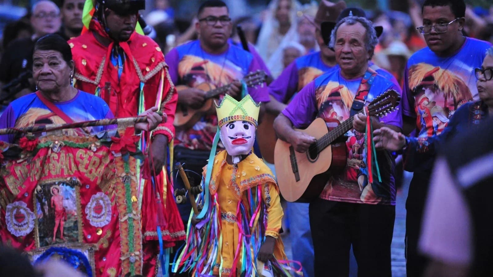 Bandeira do santo, violeiro e multidão reunida em celebração da Folia de Reis