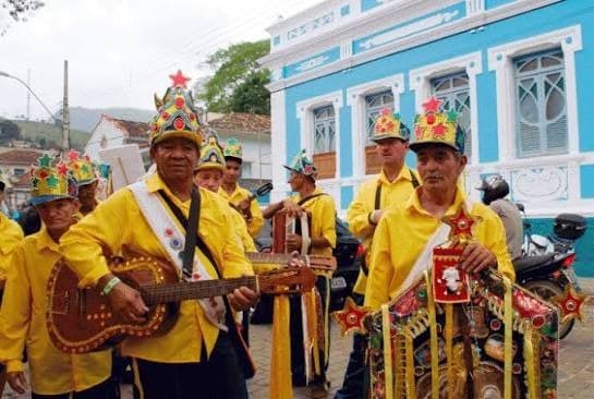 Grupo de Folia de Reis com coroas e trajes amarelos desfilando por rua de casario histórico